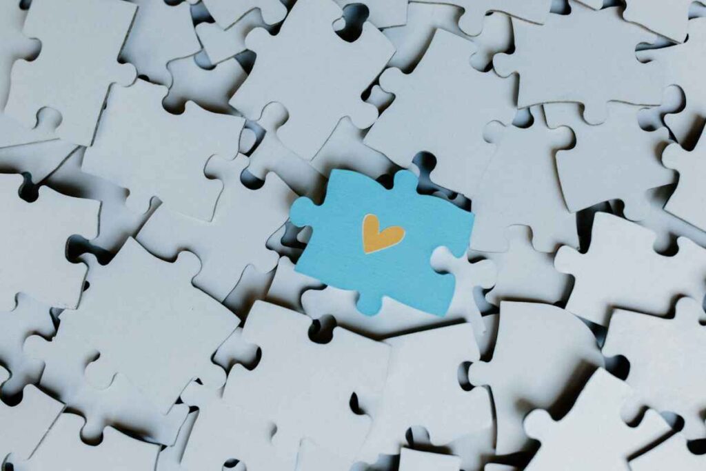 A blue puzzle piece with a heart symbol among plain white pieces, symbolizing connection with the Self in Internal Family Systems therapy.