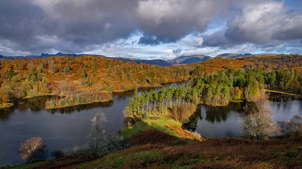 A panoramic view of a calm lake winding through rolling hills covered in autumn foliage.