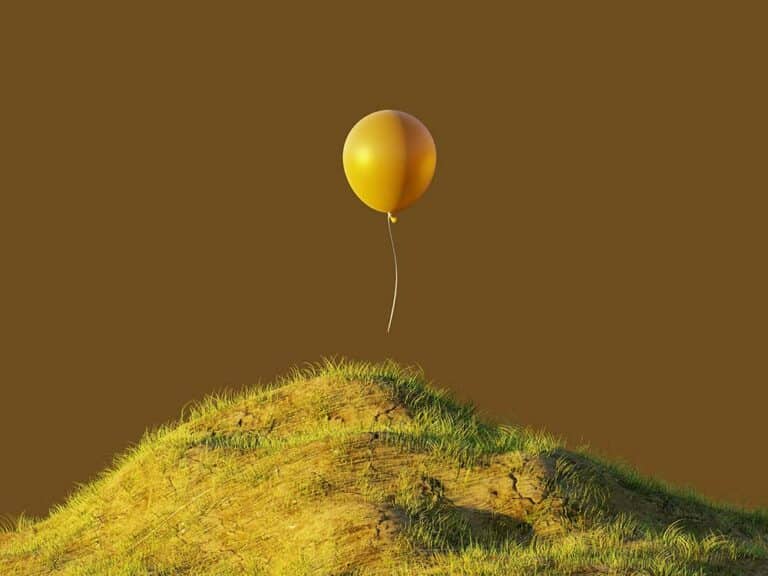 A single yellow balloon floating above a grassy hill