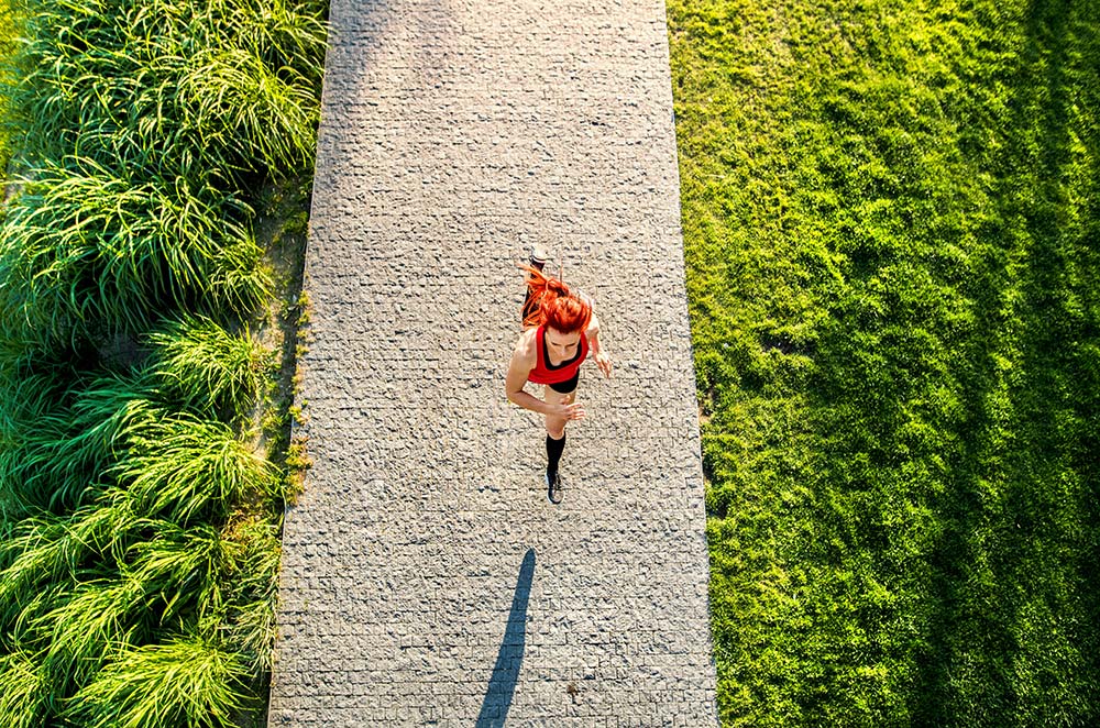 A young athlete in sportswear running on a concrete path in a sunny green park