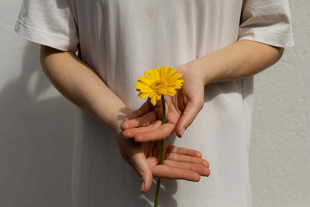 a person holds a yellow flower behind their back